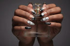 Dark-skin hands wearing black star chrome reusable press-on nails holding perfume bottle — LuxepressCo