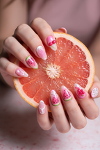 Fair skin hands wearing pink jelly fruit custom press-on nails holding fresh pink grapefruit — LuxepressCo