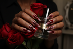 Lifestyle dark skin hands wearing crimson jelly stiletto custom press-on nails holding roses — LuxepressCo