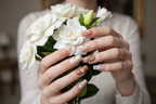 Fair-skin hands wearing ocean shell starfish marble gold bow pearl custom press-on nails holding white gardenias — LuxepressCo