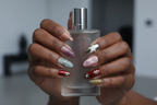 Dark-skin hands wearing chrome star silver flame Y2K almond custom press-on nails holding perfume — LuxepressCo