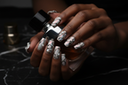 Dark-skin hands wearing dark chrome aurora reusable press-on nails holding silver black perfume bottle — LuxepressCo