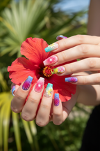 Fair skin hands wearing rainbow aurora tropical square custom press-on nails holding tropical hibiscus flower — LuxepressCo
