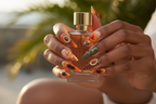 Dark-skin hands wearing tropical hibiscus leopard stiletto orange flower palm leaf custom press-on nails holding perfume — LuxepressCo