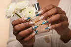 Lifestyle dark skin hands wearing teal blue peach ombre galaxy custom press-on nails holding white ranunculus — LuxepressCo