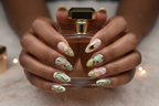 Dark-skin hands wearing sage green aurora dragonfly floral gold botanical custom press-on nails holding perfume — LuxepressCo