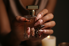Dark-skin hands wearing dark cherry tortoiseshell stiletto gold flower custom press-on nails holding perfume — LuxepressCo
