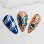 Close-up royal blue swirl marble and butterfly wing custom press-on nails with gold chrome outline — LuxepressCo