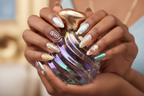 Dark-skin hands wearing aurora iridescent reusable press-on nails holding aurora gold perfume bottle — LuxepressCo
