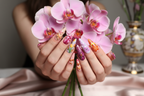 Fair-skin hands wearing orchid tulip maximalist stiletto purple pink flower custom press-on nails holding pink orchids — LuxepressCo