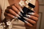 Lifestyle dark skin hands wearing ink calligraphy jelly custom press-on nails holding cherry blossoms — LuxepressCo