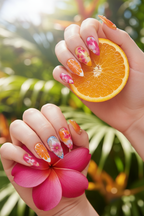 Fair skin hands wearing sunset bloom watercolor custom press-on nails holding orange slice and pink tropical flower — LuxepressCo
