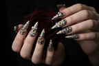 Fair-skin hands wearing steampunk biomechanical eyeball custom press-on nails holding dark burgundy-black rose — LuxepressCo