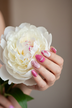 Fair-skinned hand wearing pink shell press-on nails holding white peony
