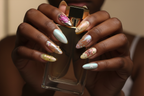 Dark-skin hands wearing holographic aurora reusable press-on nails holding gold perfume bottle — LuxepressCo