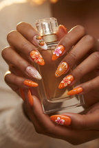 Dark skin hands wearing orange 3D floral citrus custom press-on nails holding gold perfume bottle — LuxepressCo