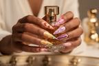 Dark-skin hands wearing orchid tulip maximalist stiletto purple pink flower custom press-on nails holding perfume — LuxepressCo
