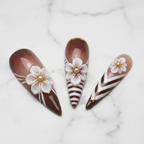 Close-up brown white chevron stripe 3D floral gold foil stiletto salon-quality nails marble background — LuxepressCo