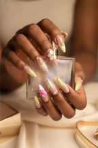 Dark-skin hands holding pearl perfume wearing nude aurora shimmer 3D plumeria reusable press-on nails — LuxepressCo
