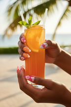 Dark skin hands wearing sunset bloom watercolor custom press-on nails holding tropical cocktail with orange garnish — LuxepressCo
