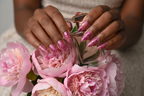 Dark-skin European hands wearing pink chrome heart coquette custom press-on nails holding pink peonies — inclusive reusable nails lifestyle — LuxepressCo