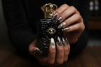 Dark-skin hands wearing gothic cat eye reusable press-on nails holding dark gothic perfume bottle — LuxepressCo