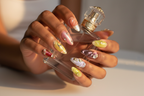 Dark-skin hands wearing aurora fairycore jelly gold star rose custom press-on nails holding perfume — LuxepressCo