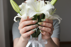 Fair-skin hands wearing sage green aurora dragonfly floral gold botanical custom press-on nails holding white lilies — LuxepressCo